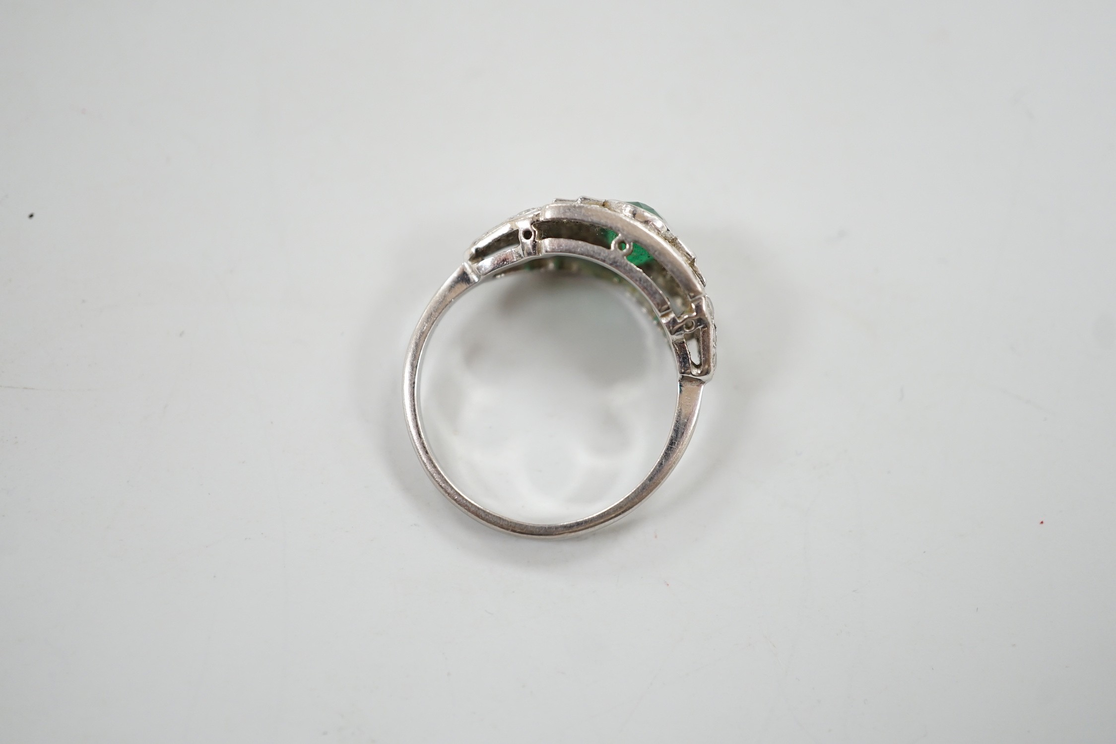 An Art Deco white metal, singe stone oval cut emerald and round and baguette cut diamond cluster set ring, size O/P, gross weight 4.2 grams.
